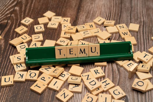 Wooden Scrabble tiles spelling TEMU on a green rack with scattered tiles on a wooden surface.